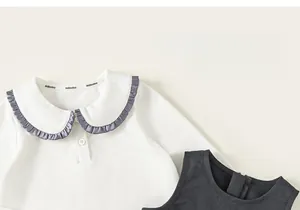 Detail eines Baby-Mädchen-Sets mit weißem Hemd mit Kragen und lila Rüschenbesatz am Ausschnitt