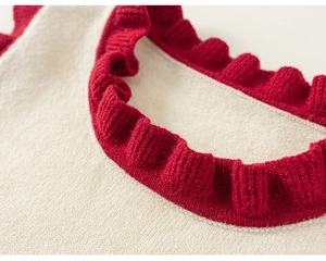 Detail of knit sweater vest with red ruffled neckline contrast on off-white fabric