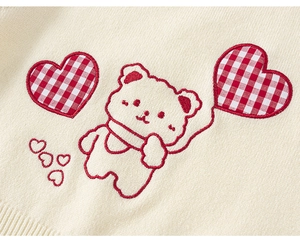Detail of cute embroidered cartoon bear and heart balloons on cream knit sweater vest