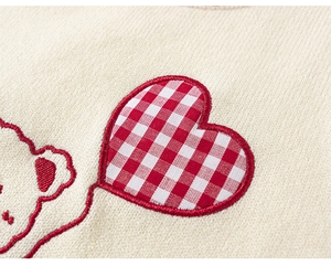 Close-up detail of knitted sweater vest showing embroidered red bear and checkered heart