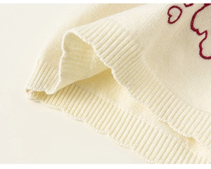 Close-up of cream knit sweater with red bear embroidery and ribbed hem detail