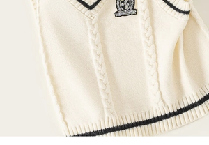 Detail of V-neck knitted vest featuring cable-stitch texture and embroidered badge