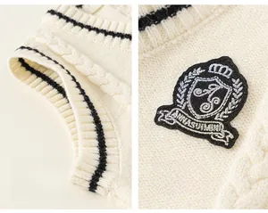 Detail of cream knit vest featuring cable knit texture, v-neck stripes, and shield embroidery