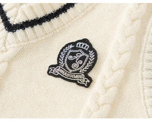 Detail of cable knit texture and embroidered school crest badge on cream sweater vest