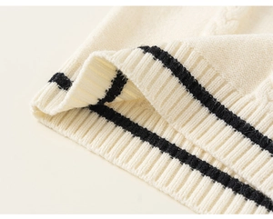 Detailed macro view of cream knitted vest featuring classic cable knit and black striped hem
