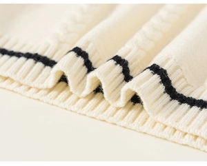 Detailed cable-knit texture of cream vest with navy blue ribbed stripe trim at the hem
