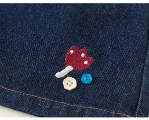 Détail macro d'une broderie champignon et boutons fleurs sur jupe denim enfant