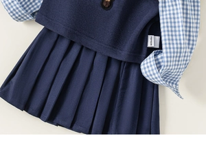 Detail view of girl's school style set with knit vest, plaid shirt and pleated skirt