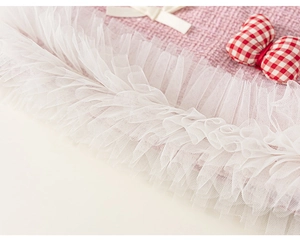 Detailed view of pink tweed fabric with layered white mesh ruffles and bow accents