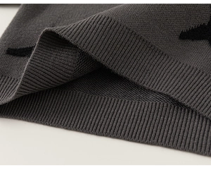 Detail of grey knitted sweater featuring ribbed hem and black star jacquard pattern