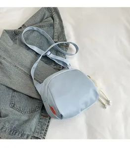 Detail view of a light blue nylon crossbody bag featuring a white plush ball charm