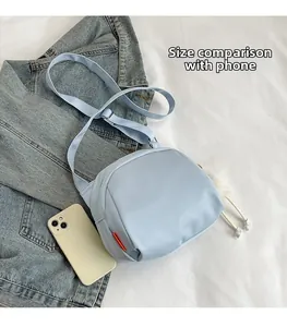 Close-up of light blue canvas shoulder bag with orange tag and phone size comparison
