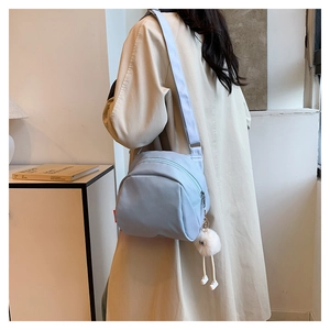 Close-up of light blue canvas crossbody bag with a cute white plush pendant accessory