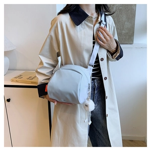 Detail of light blue nylon crossbody bag featuring a soft white plush pom-pom keychain