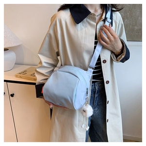 Close-up of light blue nylon messenger bag featuring a white plush pom-pom keychain