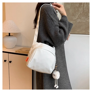 Detail view of white canvas crossbody bag with orange fashion label and plush doll charm