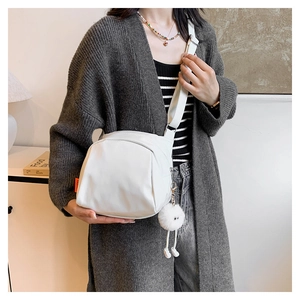 Detail view of white canvas crossbody bag featuring an orange side label and plush toy charm