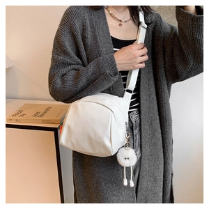 White canvas crossbody bag with plush monster charm detail shown on a grey knit cardigan