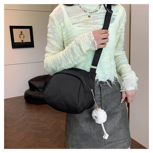 Detail of black crossbody canvas bag with white plush charm and adjustable strap