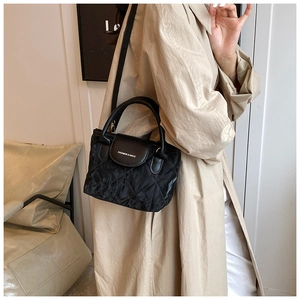 Detail of black quilted handbag with fashion lettering and satin texture on light coat