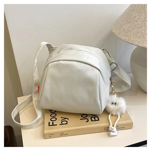 Detail shot of white triangular crossbody bag with orange tag and plush ball on a desk