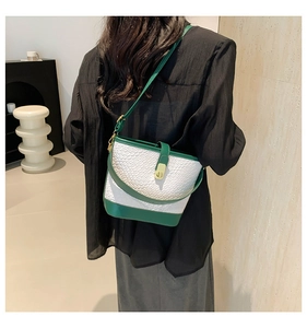 Detail of woven textured bucket bag with green leather trim and gold metal buckle