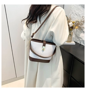 Detail of woven bucket bag with brown leather trim and golden metal clasp on a model