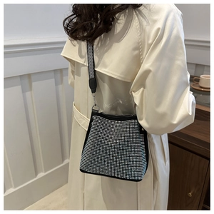 Détail du sac seau noir en strass avec large bandoulière rayée sur un trench-coat