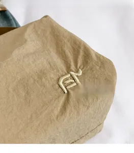 Détail macro du sac cabas en nylon kaki montrant la texture plissée et la broderie