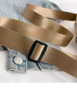 Détail d'une bandoulière en nylon kaki avec boucle noire sur fond de tissu en denim bleu