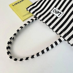 Detailed close-up of striped canvas tote bag with Leo patch and woven shoulder strap