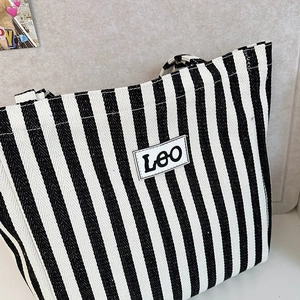 Detail of canvas tote bag with black and white vertical stripes and Leo patch logo