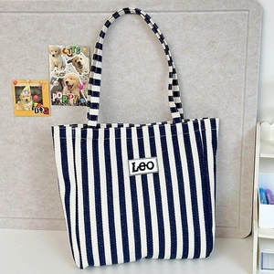 Detail of blue and white striped canvas tote bag with LEO letter patch on a white desk