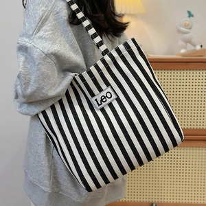 Detailed side view of a large striped canvas tote bag worn by a model in a cozy room