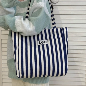Detail of blue and white striped canvas tote bag with LEO logo worn on the shoulder