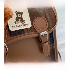 Detail shot of brown plaid woolen bag featuring leather trim and a cute bear patch