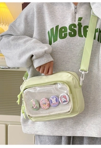 Close-up of green canvas crossbody bag featuring transparent PVC pocket and bunny badges