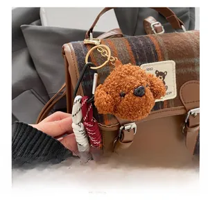 Detailed close-up of brown plush teddy dog charm with braided rope on a plaid bag