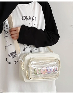 Close-up of white canvas crossbody bag with clear PVC window and four cartoon badges