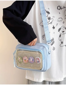Detail of light blue crossbody bag with clear window and cute rabbit badges worn by model