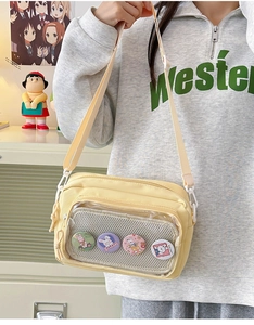 Detail of light yellow canvas crossbody bag featuring a clear pocket with cartoon rabbit badges