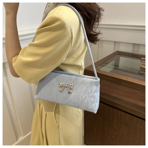 Borsa a spalla plissettata blu con fiocco argento indossata da una modella in stile moderno