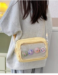 Detail of yellow canvas crossbody bag featuring clear PVC window and cartoon rabbit badges