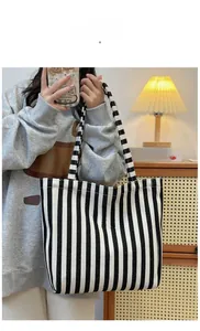 Detail of canvas tote bag featuring black and white vertical stripes and woven handles