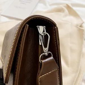 Close-up of silver metal hook and fine stitching on the dark brown leather bag side