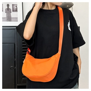 Close-up of bright orange crescent crossbody bag on model with wide strap detail
