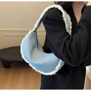 Sac croissant en denim bleu avec franges en fausse fourrure blanche porté par un mannequin