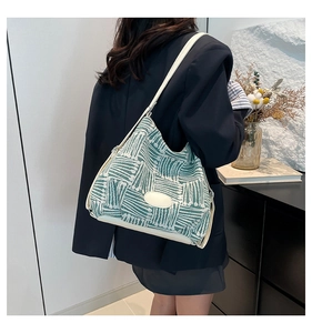 Detail of green woven shoulder bag with cream oval patch and contrast trim on model