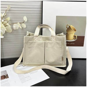 Detail of cream corduroy tote bag featuring dual front pockets and woven fashion label