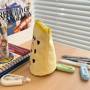Close-up of a yellow canvas cartoon pencil case standing on a desk with stationery
